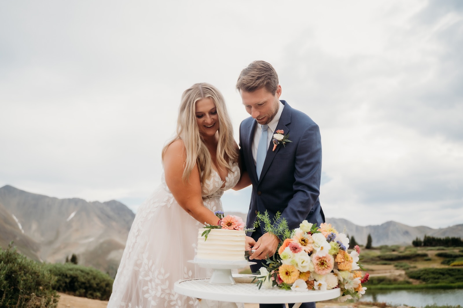 Couple cutting a small floral wedding cake in the mountains