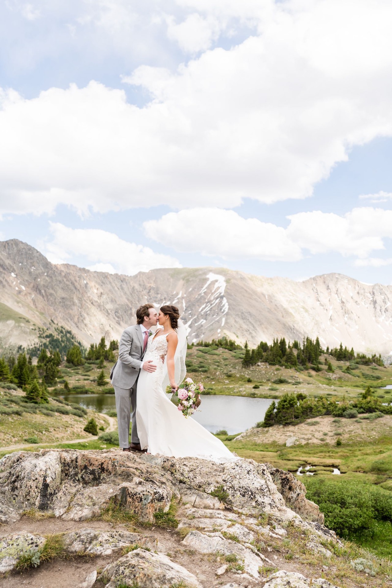 Bride and groom kissing on a rock with alpine peaks behind