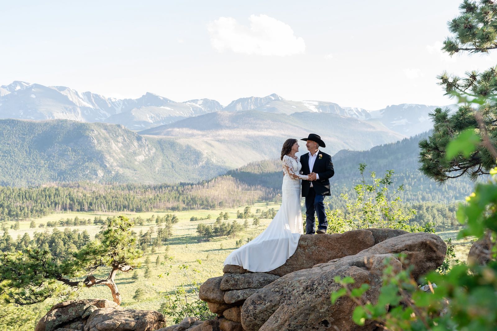 Bride and groom on a rocky overlook with Rocky Mountain peaks behind